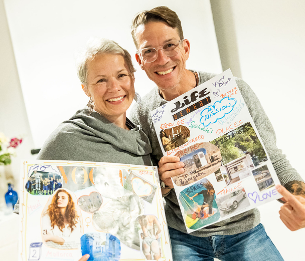 Two smiling people holding creative vision boards.