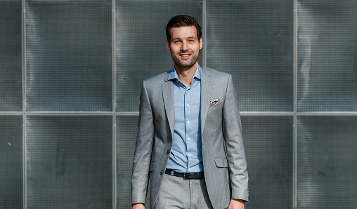 Smiling man in gray suit standing outdoors.
