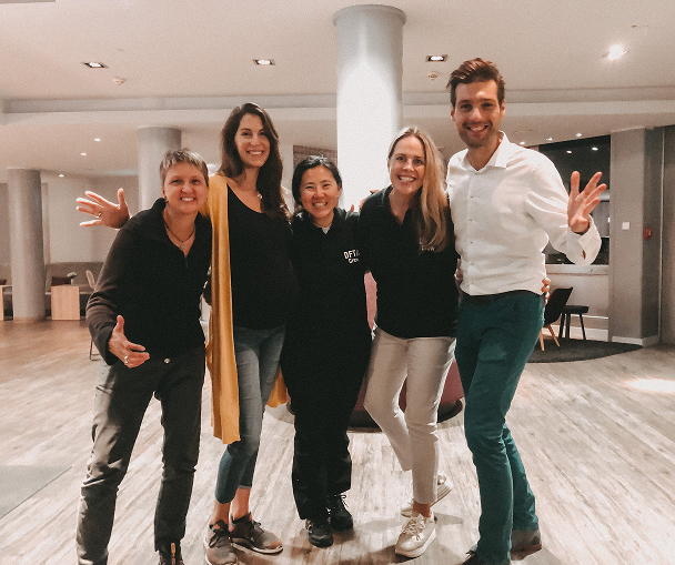 Five friends posing happily indoors together.