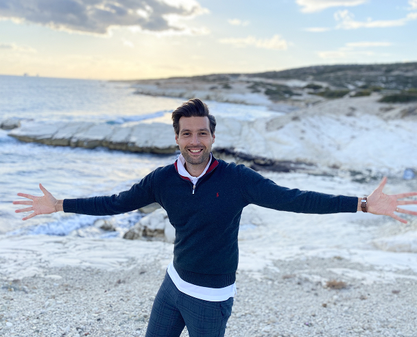Man smiling with arms wide open by the sea.