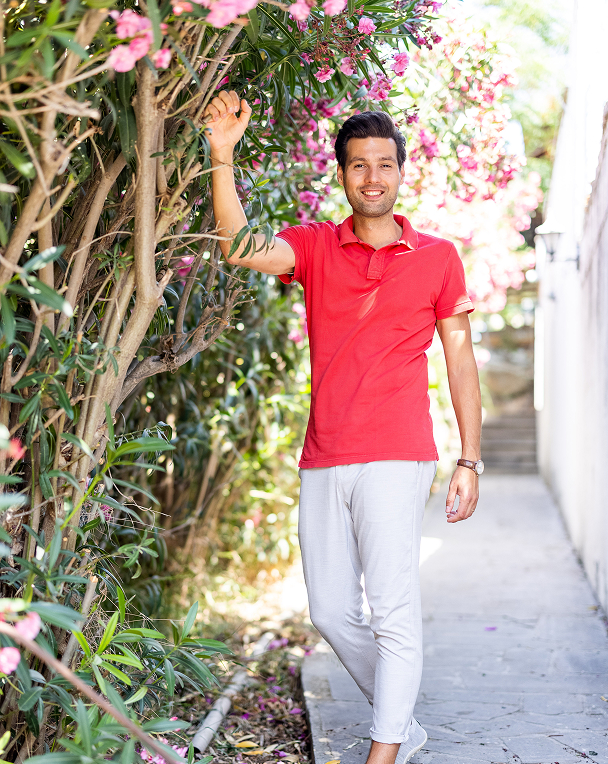 Smiling man walking in flower-lined pathway.