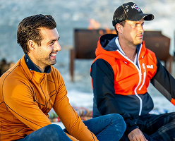 Two men sitting by a campfire outdoors.