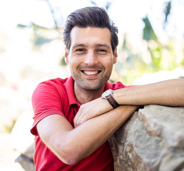 Smiling man wearing a red shirt outdoors.