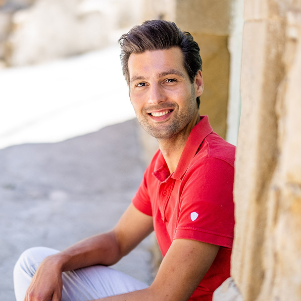 Smiling man in red shirt sitting outdoors.