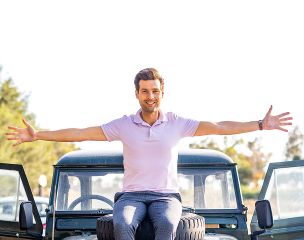 Smiling man with outstretched arms on a vehicle