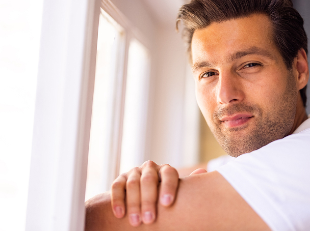 Man leaning by a window with a calm expression.
